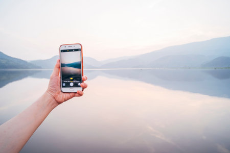 Mobile phone snapping a picture .technology in life .communication lifestyle of modern life.Female Hands Holding Smart Phone Displaying Photo of beautiful lake in Thailand .work and travelの写真素材