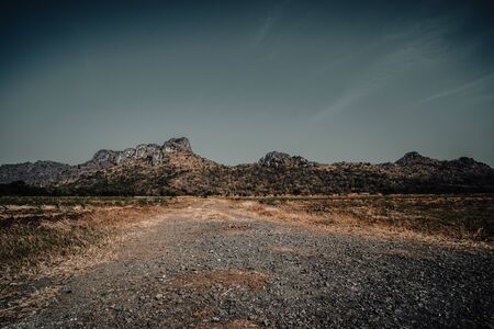 Country road in the mountains . A wide empty road in the desert toward distant mountains . gravel and dirt, sunny summer day . car road Gravel Road in mountains  as the background  in Thailandの写真素材