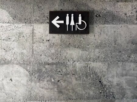 modern public toilet sign on the cement wall. Toilet icon sign on concrete wall . mens and womens disabled restroom signage with arrow made from steel plate on grey concrete wall.の写真素材