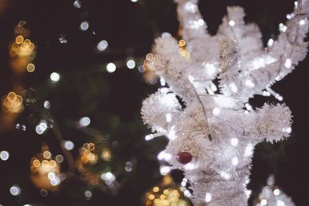 funny reindeer with lights tangled in antlers . Decorated Christmas tree on blurred background.  New Year holidays background.の写真素材