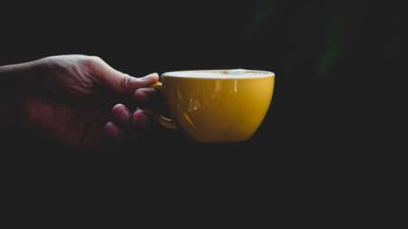 Close-up isolated hand holding yellow mug on black background. Hand hold simple yellow cup. Perfect...