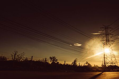 Silhouette of high voltage tower with electrical wires on sunset background. View through the grass. Power line support in a field with setting sun high-voltage power lines at sunset, high voltageの写真素材