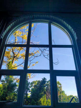 Arched window with view to autumnal landscape, bright sunshine. View through the window in autumn.の写真素材
