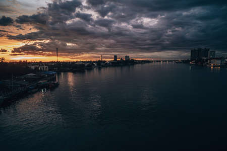 Panorama Cityscape at sunset with large river at foreground and strom clouds at background in Thailand.の写真素材