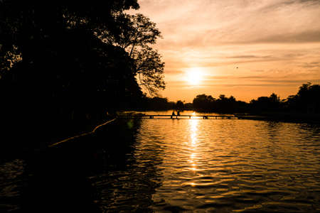 Lake landscape at sunset with Couple in love back light silhouette at lake orange sunset. Loving couple watching beautiful sunsetの写真素材