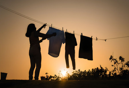 A peaceful silhouette of a person hanging laundry during golden hour, bathed in warm sunlight, evoking nostalgia and simplicity.の素材