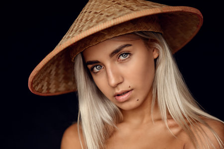 fashion photo of beautiful woman with blonde hair and expressive eyes posing with asian style wicker...