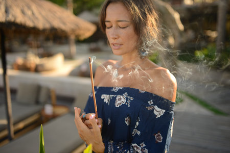 fashion photo of beautiful woman with short brunette hair posing with close eyes and smoke incense on asian background in Baliの写真素材