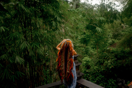 fashion photo of beautiful woman in long bright indian roach and blue boho clothes posing on the wood verande in tropical Jungle background in Baliの写真素材