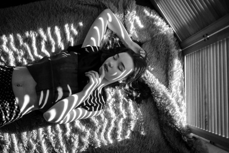 fashion black and white photo of beautiful woman with brunette hair in dark clothes posing in shadow stripes in studioの写真素材