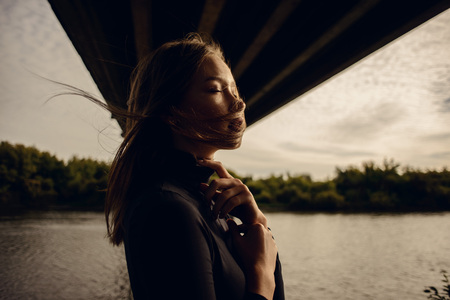 fashion outdoor photo of beautiful woman with brunette hair in casual dark clothes walking near bridge under riverの写真素材
