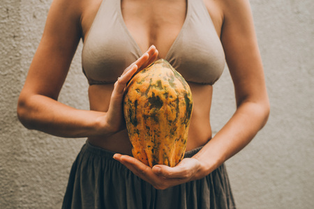 Beautiful photo of woman in boho clothes keep the tropical fruit papaya in hands on the light background in Baliの写真素材