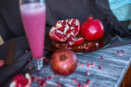beautiful photo of still life of healthy cocktail of fresh pomegranate juice and almond milk in hight glass served with fresh red pomegranate on dark background.の写真素材