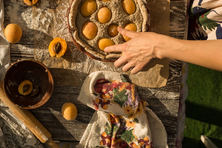warm light photo of outside a woman in gentle sundress cooking a sweet pie with fresh apricots on a sunny summer dayの写真素材
