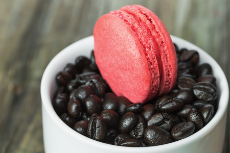 macaroons in white cup with coffee beans on wooden tableの写真素材