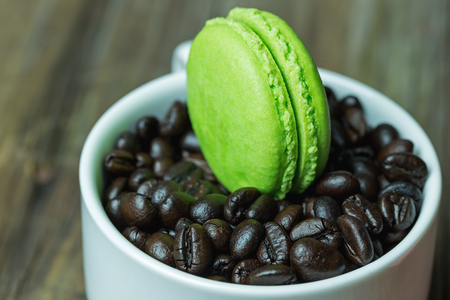macaroons in white cup with coffee beans on wooden tableの写真素材