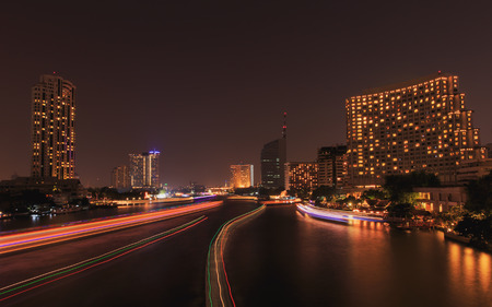 traffic in the river on night city skyline background, long exposure used, lighting on boat making light tails.の写真素材