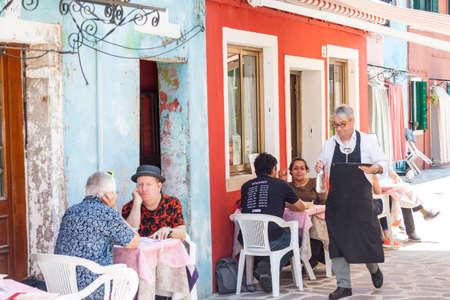 Burano, ITALY -  MAY 2, 2019: Tourist in street restaurant old Colorful city of Burano on May 2,2019 in Burano island in Italy. View on Colorful houses.のeditorial素材