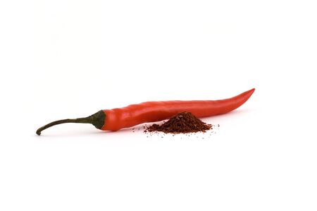 Chili pepper with spilled original chili spice next to it on white background, focus at near end of pepperの写真素材