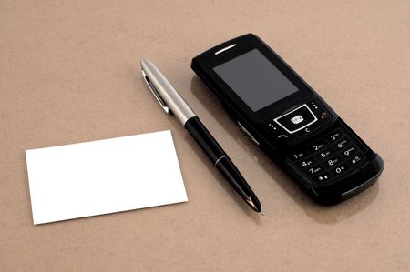 Mobile phone with pen and blank business card at brown deskの写真素材
