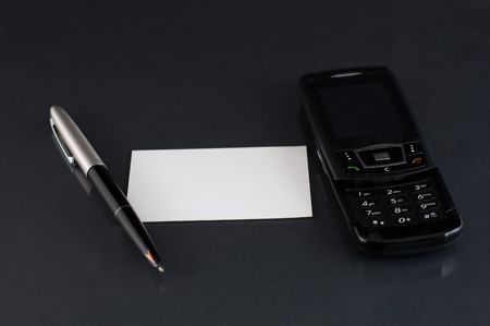 Mobile phone with pen and blank business card at black desk with small reflectionの写真素材