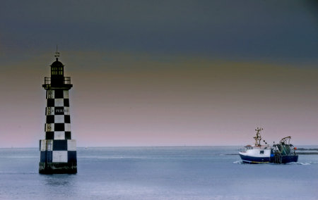 Lighthouse and fishing boat in the ocean on a cloudy day.の写真素材