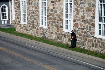 A man with a lawn mower walks along the street on a sunny day.