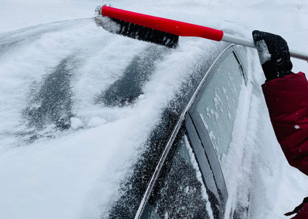 Man cleaning snow from the windshield of his car with a brush.