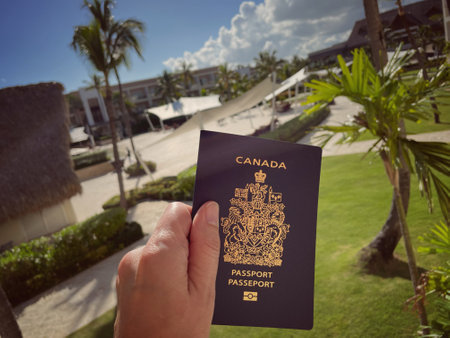 hand holding a Canadian passport against a background of palm trees and tropical plantsのeditorial素材