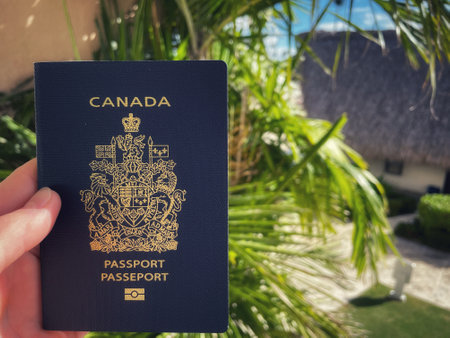 hand holding a Canadian passport against a background of palm trees and tropical plantsのeditorial素材