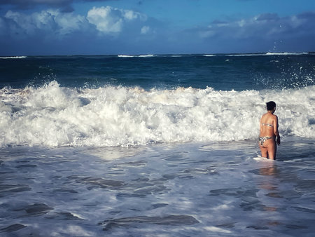 Woman in bikini on the beach looking at the waves of the ocean