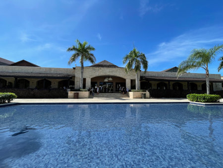 Swimming pool at luxury villa with palm trees and blue sky. Luxury hotel. Guests at a resort wait outside a restaurant. The Royalton Punta Cana swimming pool in the foregroundのeditorial素材