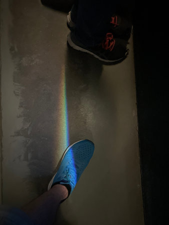 Man wearing blue sneakers with a rainbow on the floor