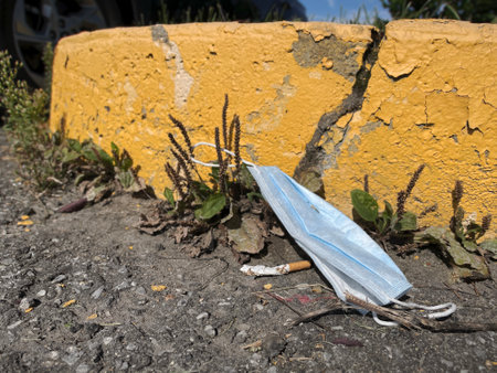 A discarded medical mask lies on the ground near a broken yellow wall.の写真素材