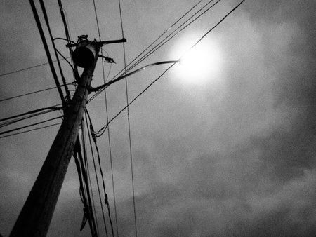 Black and white photo of electric pole with the sun shining through itの写真素材