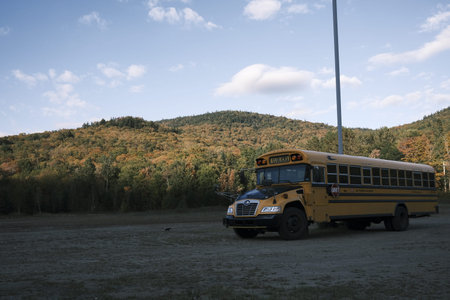 School bus in a field with autumn trees and mountains in the background