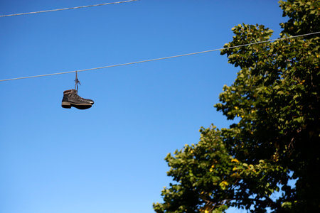 A pair of black shoes hanging on a wire on a blue sky backgroundの写真素材