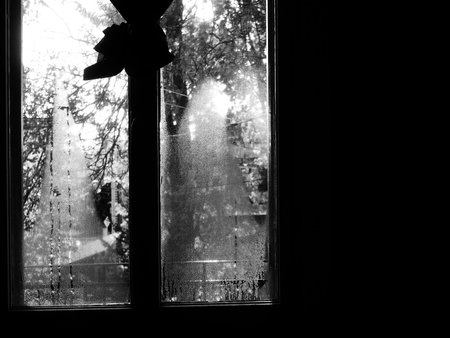 A black and white photo of a window with a blurry background. Humidity on the window, view from...