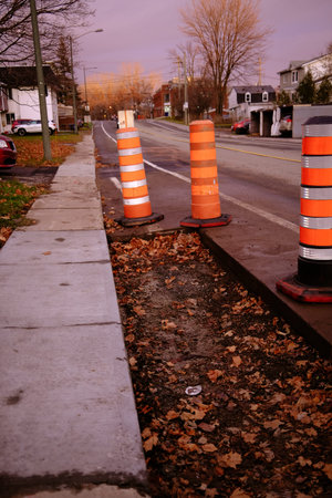 Traffic cones on a sidewalk with fallen leaves in the foreground.