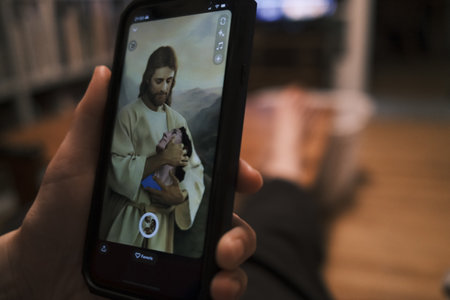 A close-up of a man holding a mobile phone with a picture of Jesus Christ on the screen.のeditorial素材