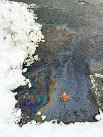 Melting snow on the road in winter, closeup of photo. A puddle of gasoline on the asphalt in winterの写真素材