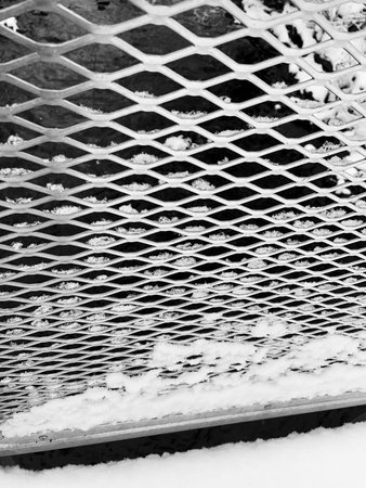Close up of a white metal grid in the snow. Black and white
