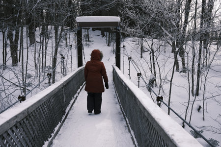 A woman in a red jacket walks along a pedestrian bridge in winter.の写真素材
