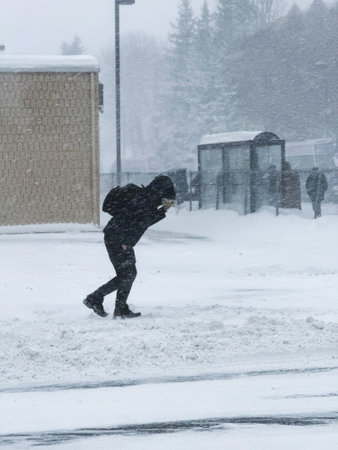 A man in a black jacket and jeans is walking through the snow.の写真素材