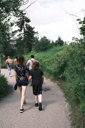 A group of young people walk along a path in the park. A mother holds her teenage boy's hand.の写真素材