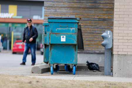 Garbage can on the street with a man walking the background.