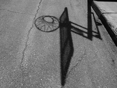 Shadow of a basketball hoop on the asphalt. Black and white street photography.