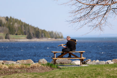 A man sitting on a bench and playing guitar by the riverのeditorial素材