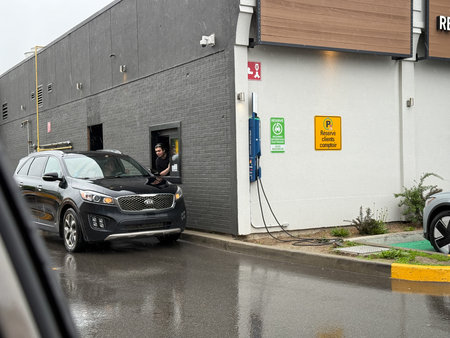 A person answers a drive-thru restaurant. An electric car charging station is on the wall of a...