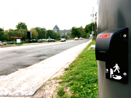 A pedestrian priority call button on a metal column for crossing the street.
